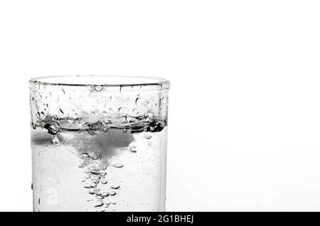 Un bicchiere d'acqua e ghiaccio su sfondo bianco.primo piano di bolle d'aria in acqua minerale. Foto Stock