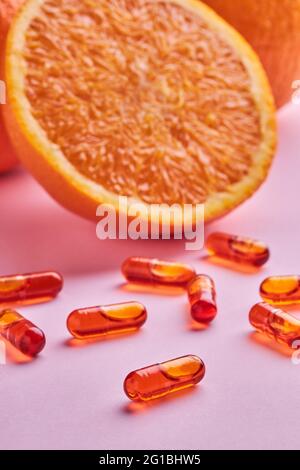 Composizione di arance tagliate mature disposte su superficie rosa vicino a pillole sparse in studio luce Foto Stock