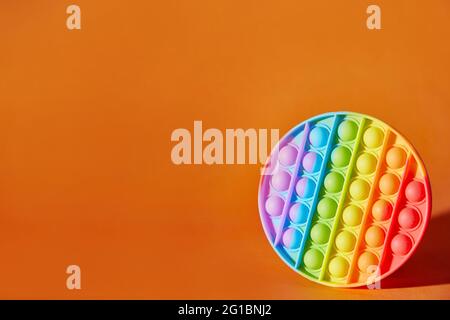 Schioccare il giocattolo su sfondo arancione con spazio per la copia. Popolare giocattolo anti-stress in silicone multicolore. Foto Stock