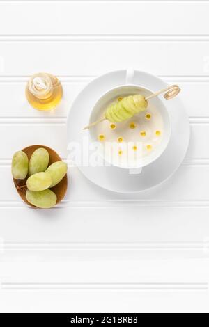 Zuppa spagnola tradizionale ajo-blanco, con uve verdi e gocce di olio d'oliva. Sfondo bianco, vista sopra la testa, posa flay. Foto Stock