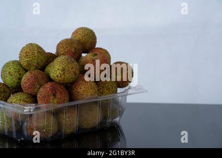 Un mazzo di lychee verdi mature in contenitore di plastica. Punti di messa a fuoco selettivi. Sfondo sfocato Foto Stock