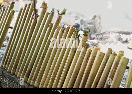 Una fila di lemang alla fine del processo di cottura. Lemang e' un cibo malese tradizionale di base durante il festival eid. Messa a fuoco selettiva. Sfondo sfocato Foto Stock