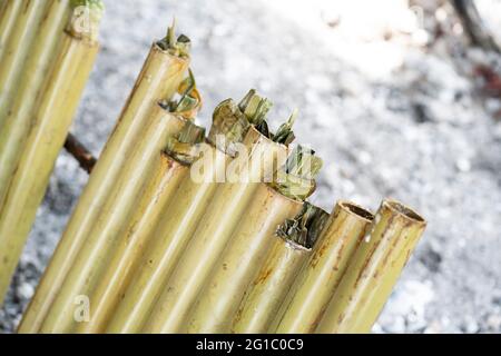 Una fila di lemang alla fine del processo di cottura. Lemang e' un cibo malese tradizionale di base durante il festival eid. Messa a fuoco selettiva. Sfondo sfocato Foto Stock