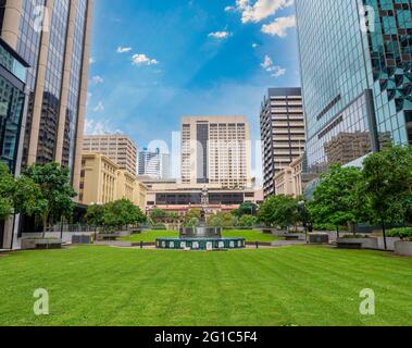 Parcheggia presso l'ufficio postale di Brisbane, Australia. Erba verde, alberi, cielo blu, hotel e uffici. Stazione ferroviaria centrale sullo sfondo. Foto Stock