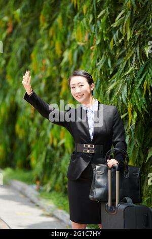 Sorridente giovane donna che agita con la mano quando si cerca di prendere un taxi auto per il terminal dell'aeroporto Foto Stock