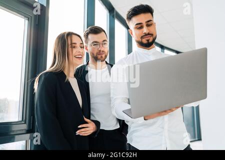 Tre impiegati che guardano a un notebook che parla del tasso di crescita dell'azienda Foto Stock