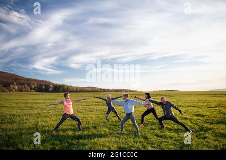 Gruppo di anziani con istruttore sportivo che fa esercizio all'aperto in natura, stile di vita attivo. Foto Stock