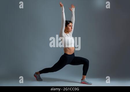 Donna in Langing Warrior posa con le braccia tese su sfondo grigio Foto Stock