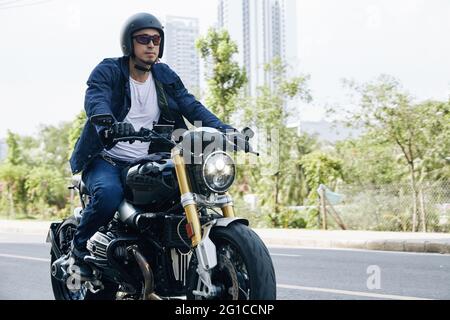 Uomo in occhiali da sole e casco che cavalcano velocemente in moto su autostrada Foto Stock