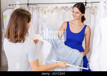 Ragazza che sceglie vestito bianco con l'aiuto di assistente Foto Stock