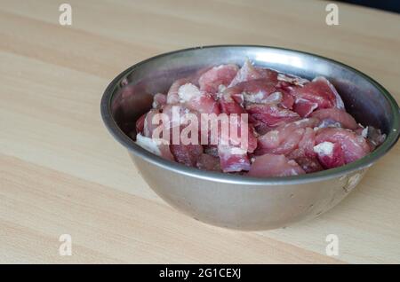 Preparazione graduale del prosciutto tagliato in casa. Fase 1: Salatura della carne per il prosciutto. Una ciotola di pezzi di carne, sale, aglio e pepe sulla tavola Foto Stock