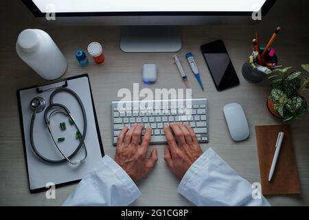 Medico che compila i documenti online e verifica i test medici dei pazienti alla scrivania del suo ufficio, vista dall'alto Foto Stock