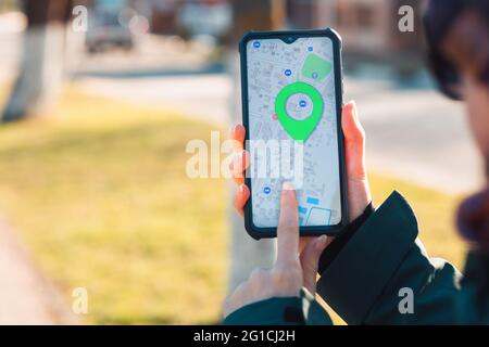 Una mano femminile tiene un cellulare con l'app online Maps aperta e mostra il luogo segnato sulla mappa.il concetto di navigatori online e tecnologia moderna Foto Stock