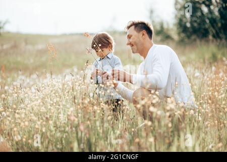 Padre trascorre del tempo con il figlio piccolo nella foresta sul prato con fiori, gli racconta delle piante Foto Stock