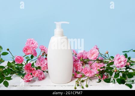 bottiglia con shampoo o gel doccia e fiori rosa rose su sfondo blu, prodotti per la cura del corpo e prodotti di bellezza Foto Stock