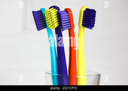 Set di spazzolini multicolore in plastica - verde, blu, rosso, viola - in vetro trasparente su sfondo bianco. Coppa con quattro colori vivaci così Foto Stock