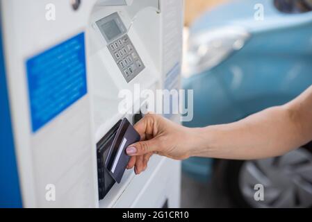 Una donna riempie la sua auto con benzina ad una stazione di benzina self-service e paga con una carta di credito ad una macchina Foto Stock