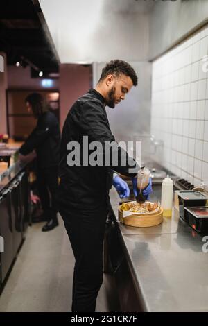 Cameriere giovane maschio che prepara il cibo al ristorante Foto Stock