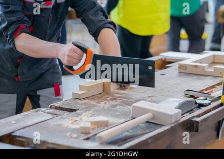 Uomo falegname usando la sega a mano per tagliare il legno sul banco da lavoro - primo piano Foto Stock