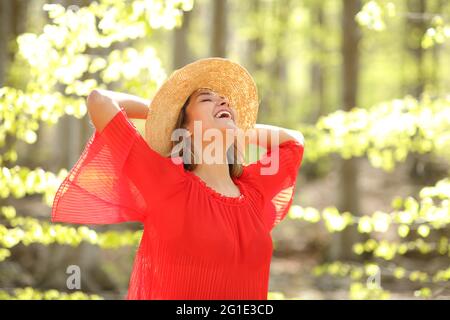 Donna eccitata in rosso che respira aria molto fresca con le braccia sulla testa in una foresta Foto Stock