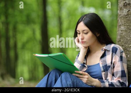 Studente asiatico che studia le note di lettura seduti appoggiandosi su un albero in un parco Foto Stock