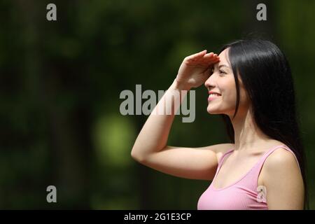 Vista laterale ritratto di una donna asiatica felice che guarda la protezione dal sole in un parco Foto Stock