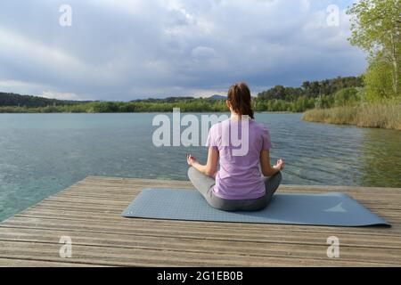 Indietro Vista ritratto di una donna che fa esercizio di yoga in un bellissimo molo lago tranquillo Foto Stock