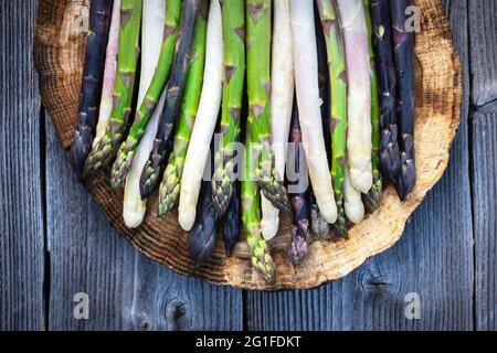 Germogli di asparagi verdi, viola e bianchi su tavola di legno. Vista dall'alto in piano. Fotografia alimentare Foto Stock