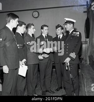 Anni '60, storico, congratulazioni .... un capitano Royal Naval decorato con la spada, scuotendo le mani con un giovane orgoglioso, in piedi insieme con altri tre membri maschi della Brigata Boys in una cerimonia di premiazione, Fife, Scozia, UK. Fondata a Glasgow, in Scozia, da William Alexander Smith nel 1883, per combinare perforazione e divertimento con valori cristiani, la Brigata dei ragazzi è la più grande organizzazione giovanile cristiana in uniforme del Regno Unito. L'introduzione del campeggio per adolescenti da parte di Alexander Smith fu qualcosa di nuovo alla fine del XIX secolo, con il primo campo BB a Tighnabruiach nel 1886. Foto Stock