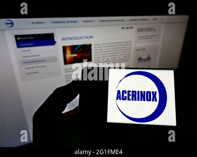 Persona che tiene il cellulare con il logo del produttore spagnolo di acciaio Acerinox S.A. sullo schermo di fronte alla pagina web aziendale. Mettere a fuoco il display del telefono. Foto Stock