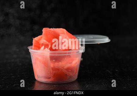 Radice di zenzero tagliata a fette sottili di colore rosso in un vaso di plastica di consegna. Messa a fuoco selettiva. Foto Stock
