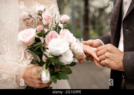 vista tagliata della donna con bouquet di nozze vicino allo sposo mettendo l'anello di nozze sul suo dito Foto Stock