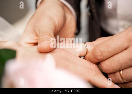 vista ritagliata dell'uomo che mette l'anello di nozze sul dito della sposa, primo piano sfocato Foto Stock