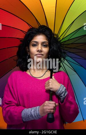 Bella ragazza Sri Lanka posa in piedi con sfondo giallo luminoso Appeso un ombrello colorato - la giovane donna sorride Foto Stock