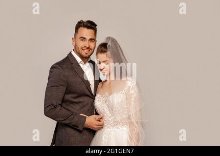 uomo felice sorridente a macchina fotografica vicino affascinante sposa isolato su grigio Foto Stock