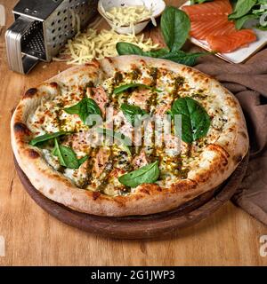 Pizza con mozzarella, salmone, spinaci, origano e pesto. Pesce pizza italiana su sfondo ligneo. Pranzo fast food per un'azienda di picnic, foto in Foto Stock