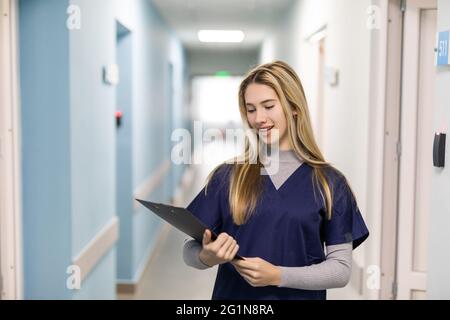 Ritratto di donna sorridente infermiera che indossa scrub in piedi in corridoio ospedale tenendo appunti Foto Stock