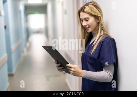 Ritratto di donna sorridente infermiera che indossa scrub in piedi in corridoio ospedale tenendo appunti Foto Stock