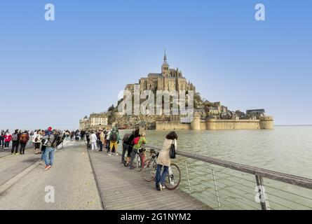 Francia, Manica (50), Baie du Mont-Saint-Michel, patrimonio mondiale dell'UNESCO, il Mont circondato dall'acqua dal ponte pedonale durante un'alta marea, i turisti guardare lo spettacolo e attendere la caduta della marea per passare Foto Stock