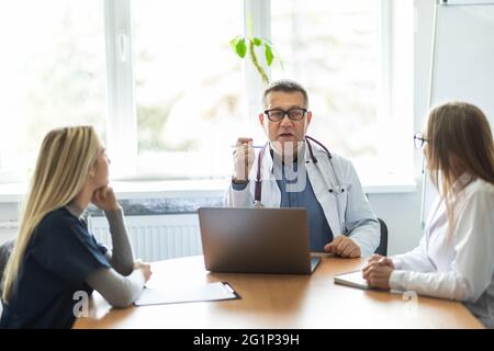 Team di personale medico che si riunita al mattino in sala riunioni in ospedale Foto Stock