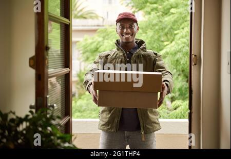 Sorridente uomo di consegna africano che tiene i pacchetti a una porta d'ingresso Foto Stock