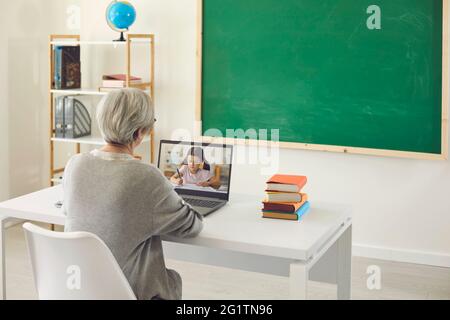 Formazione online per i bambini. Una insegnante femminile con i capelli grigi insegna una piccola studentessa ha una videochiamata portatile in classe. Foto Stock
