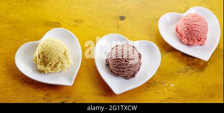 Dall'alto composizione di colorati scoop di vaniglia e cioccolato e gelato alla fragola serviti in ciotole a forma di cuore Foto Stock