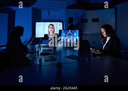 Colleghi che lavorano su computer portatili durante una conferenza online in un ufficio buio Foto Stock