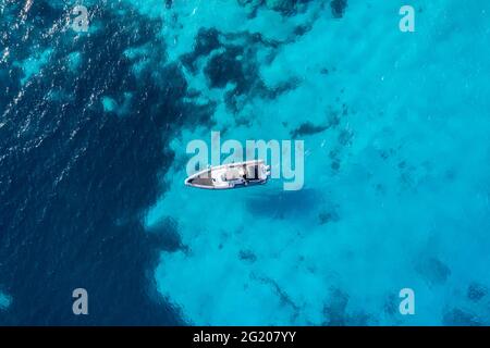 Imbarcazione gonfiabile su fondo mare di colore turchese blu. Vista dall'alto del drone aereo. Motoscafo che naviga lentamente su acqua increspata. Crociera nel Mar Egeo, Foto Stock