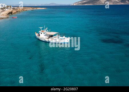 Barca da pesca su sfondo mare turchese di colore blu. Vista aerea del drone. Tradizionale peschereccio ormeggiato in acque calme dell'Egeo, giorno di sole. Grecia, Koufonisi Foto Stock
