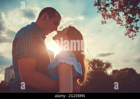 Felice coppia in amore abbracciare e sorridere in primavera parco al tramonto. Data romantica Foto Stock