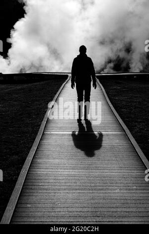 Silhouette di un singolo turista che cammina sul lungomare con vapore che sale Foto Stock