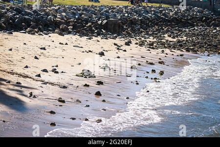 Onde dolci che lambono pacificamente il bordo di una sezione di spiaggia rinforzata di riprap sull'isola di Coronado vicino San Diego in California con sunli scintillanti Foto Stock