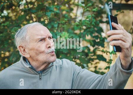 gray man prende un selfie dal suo telefono cellulare per pubblicarlo sui social media per la comunicazione. Un uomo di 88 anni comunica con i suoi nipoti Foto Stock